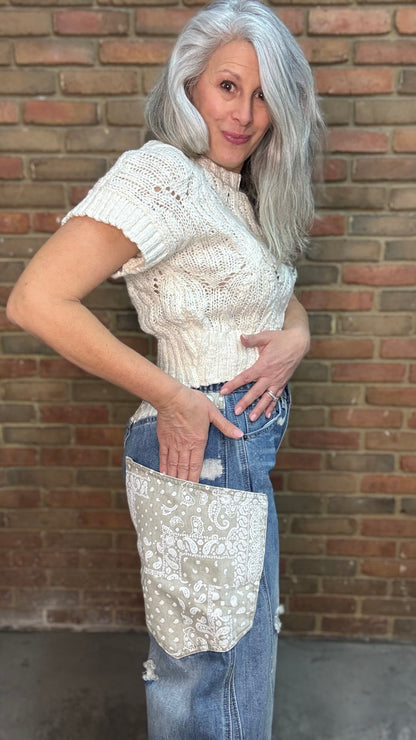 Woman standing in front of a brick wall wearing the Big Pocket Denim Pants and the Oatmeal Sweater Top.
