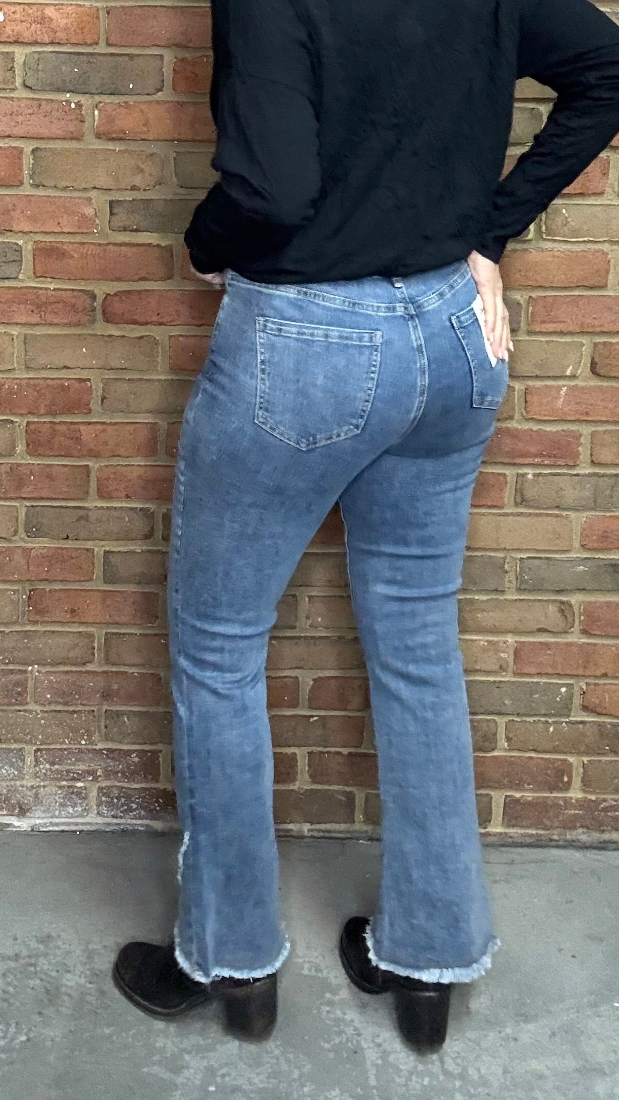 Person wearing The Front Tulip Hem Bootcut Pant jeans standing against a brick wall.