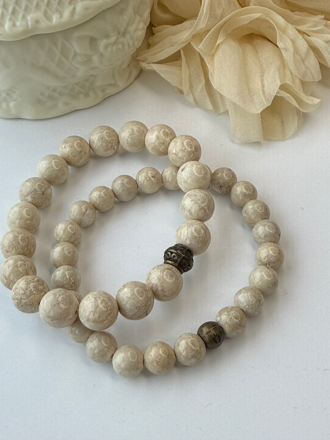 Beige beaded bracelet on a white surface with a decorative beige object.
