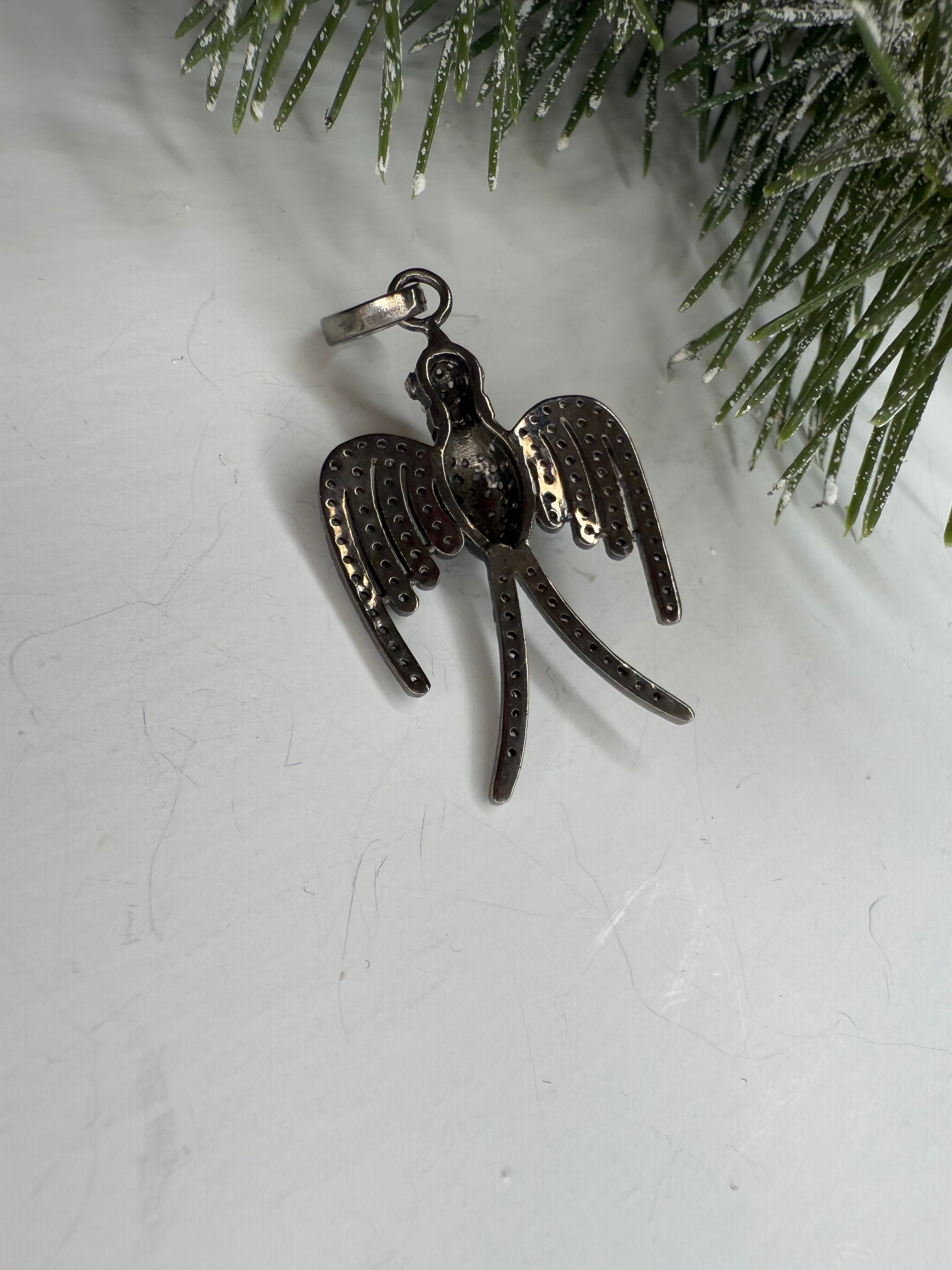 Back of bird shaped pendant with wings on a textured white background.