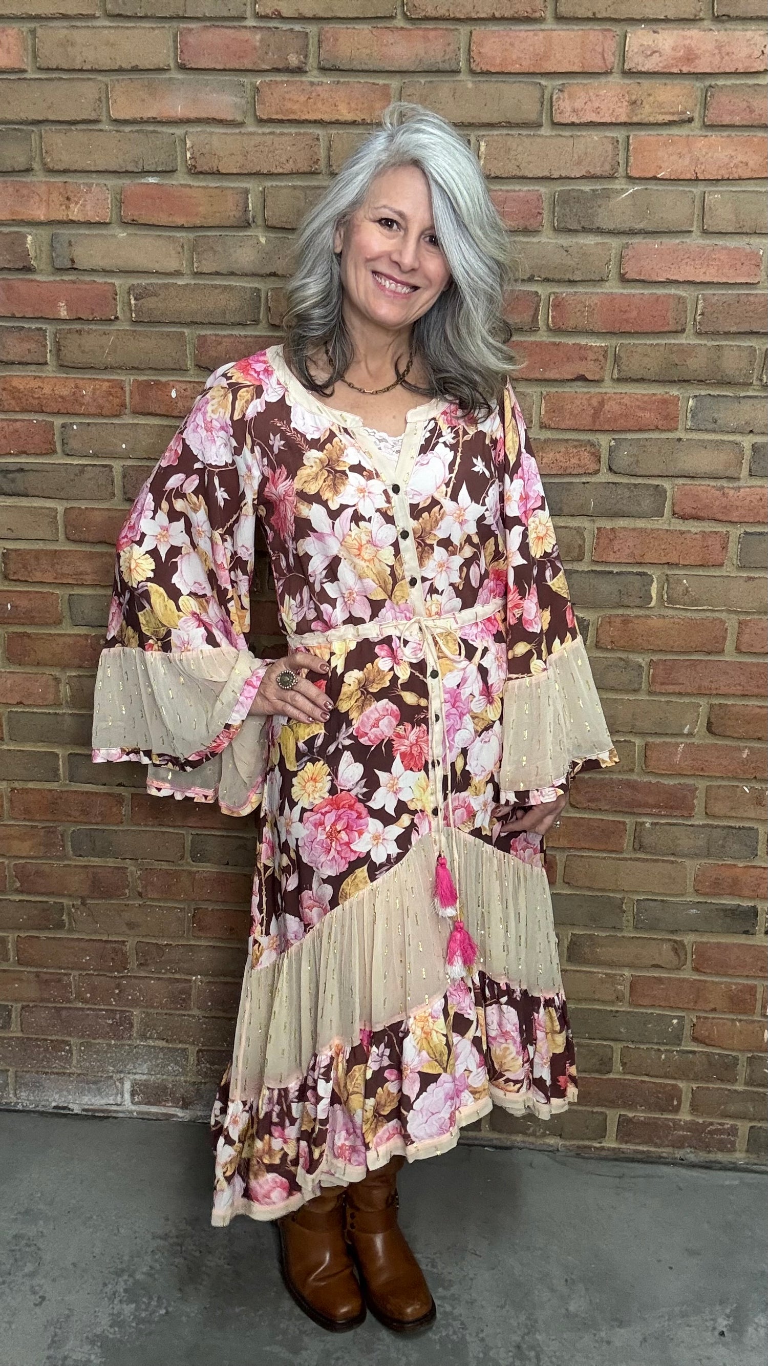 Woman wearing a floral dress standing against a brick wall.