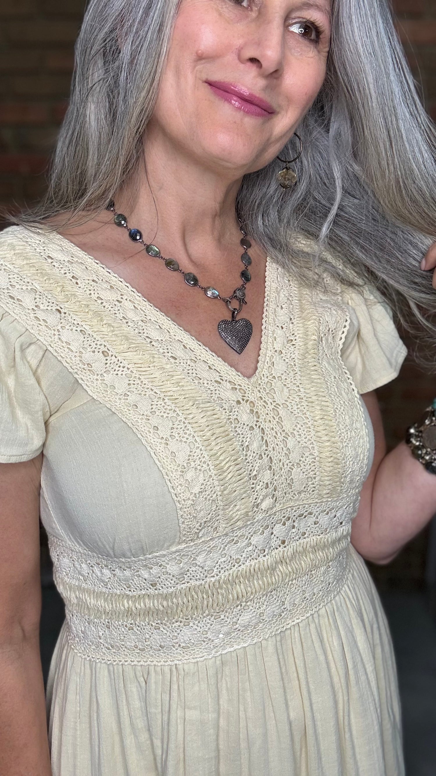 Woman in the Vina Cotton Lace Dress in Ivory standing against a brick wall