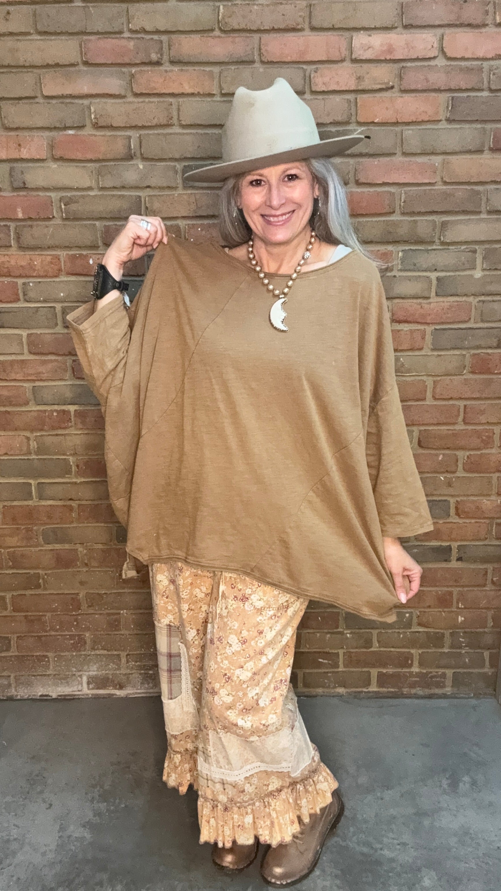 Woman wearing Be Free Top - Vintage Latte and patterned pants against a brick wall.