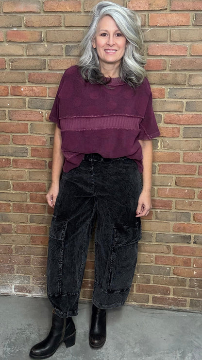 Person wearing a purple top and black pants standing against a brick wall.
