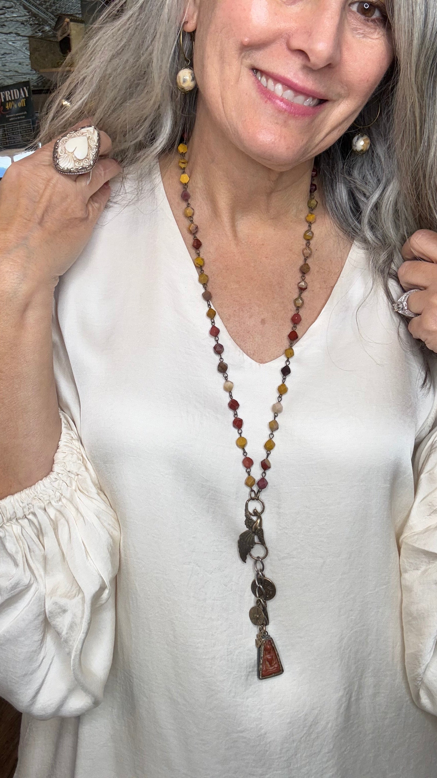 Woman wearing a white blouse with a long beaded necklace indoors.