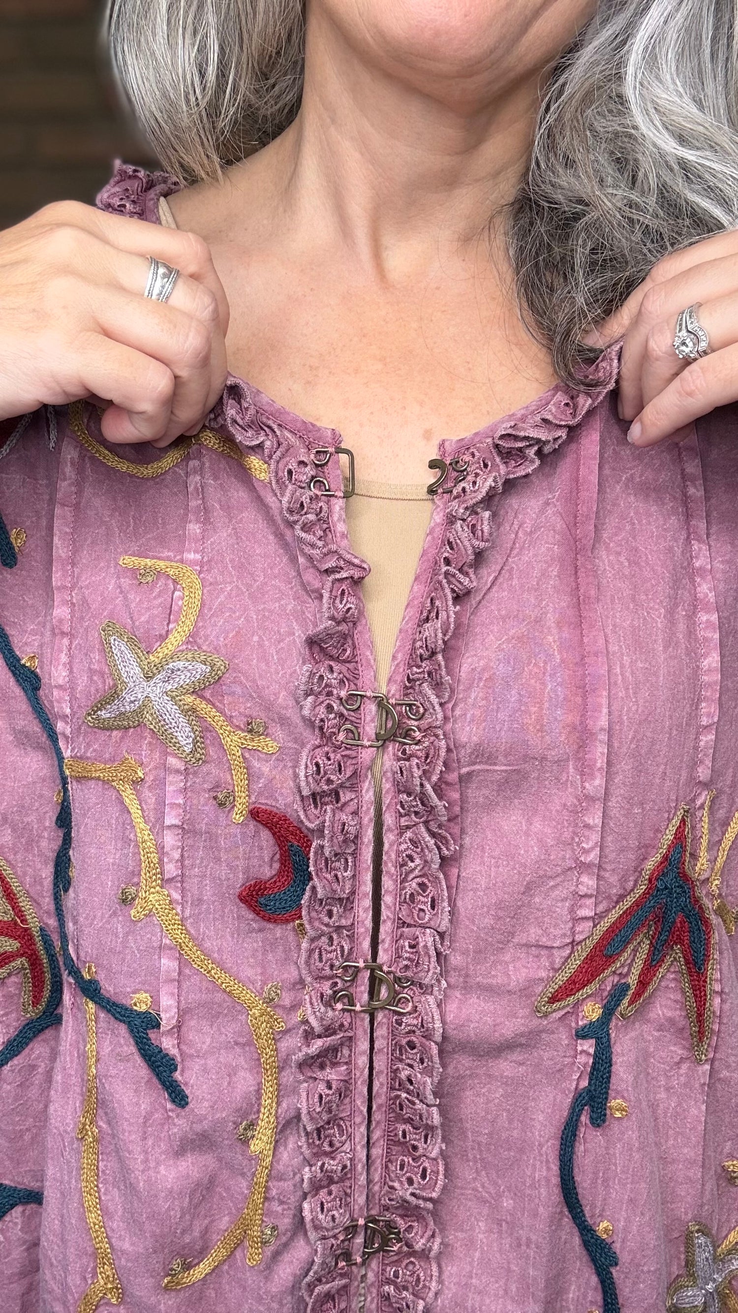 Close-up of a person wearing a pink embroidered top with colorful patterns.
