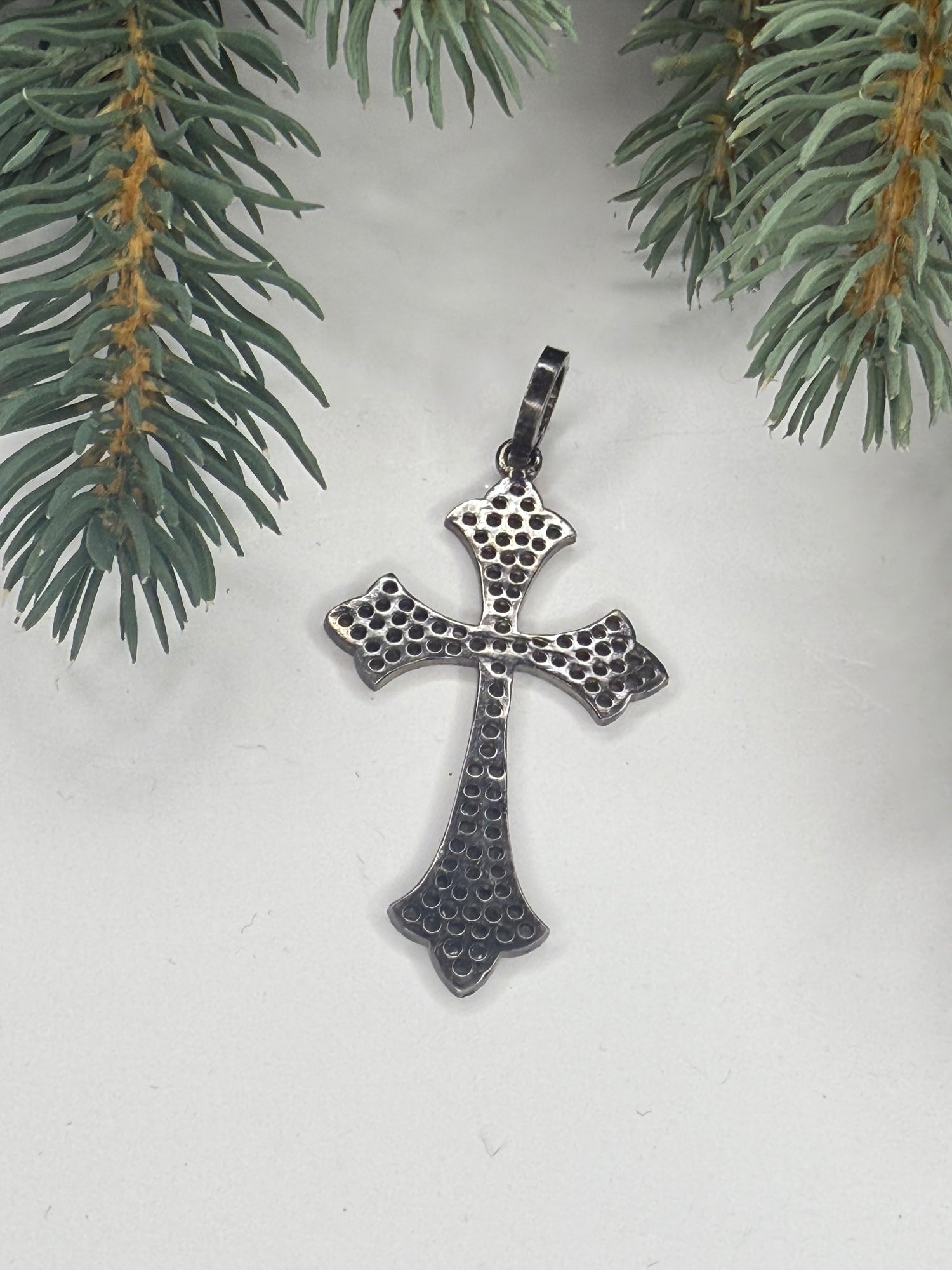 Back of cross pendant on a white background with green pine branches.
