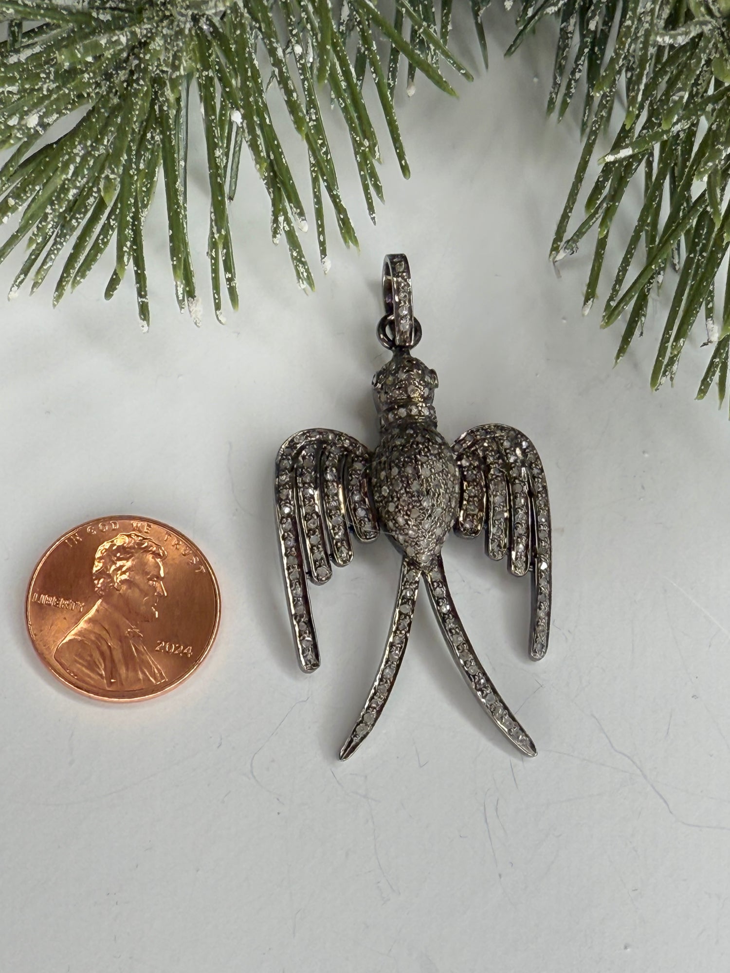 Bird shaped pendant next to a penny on a white surface with greenery.