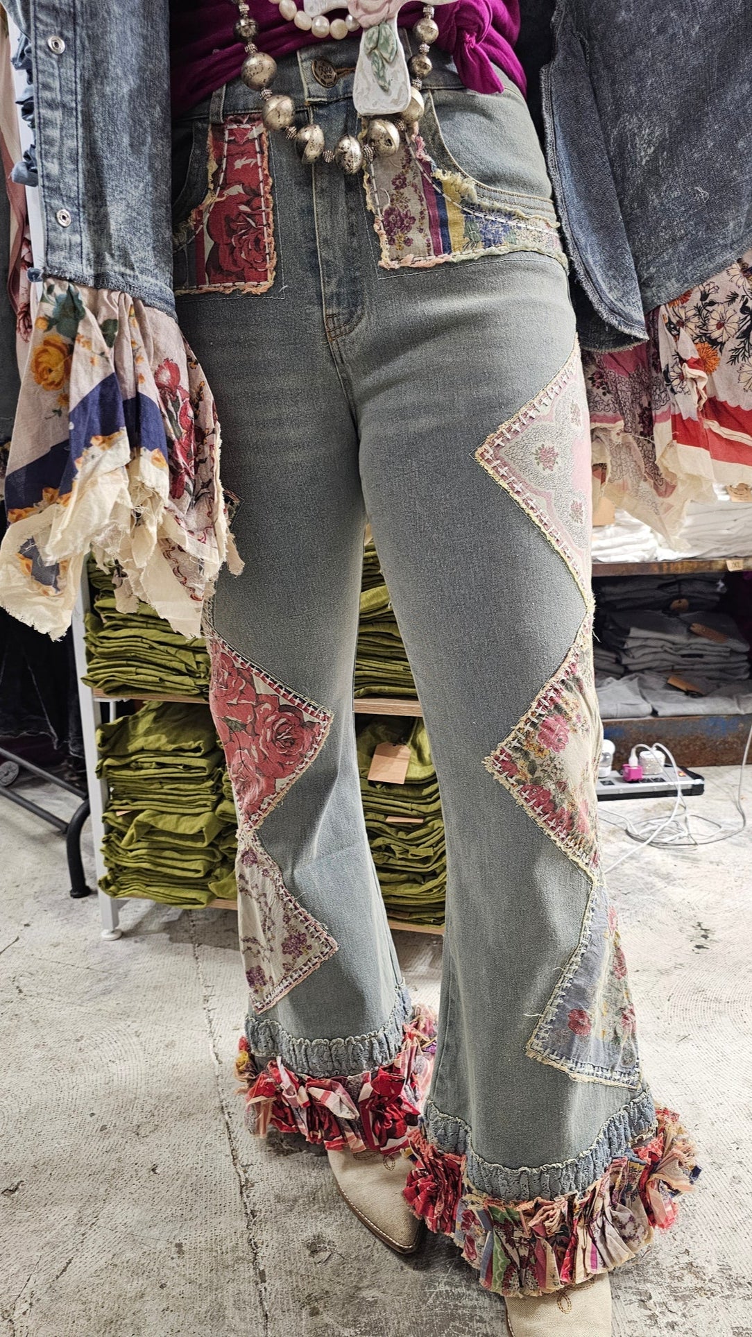 Person wearing patchwork jeans with floral patterns and ruffles in a store setting.