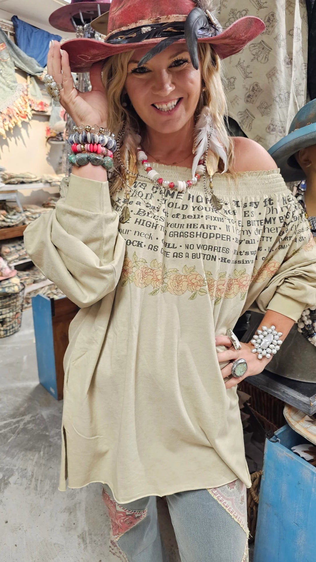 Woman wearing a beige off-shoulder top with text and graphics, standing in a market setting.