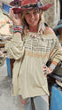 Woman wearing a beige off-shoulder top with text and graphics, standing in a market setting.