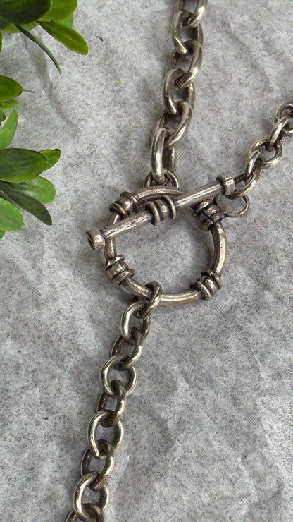 Silver chain with a clasp on a gray surface with green leaves.