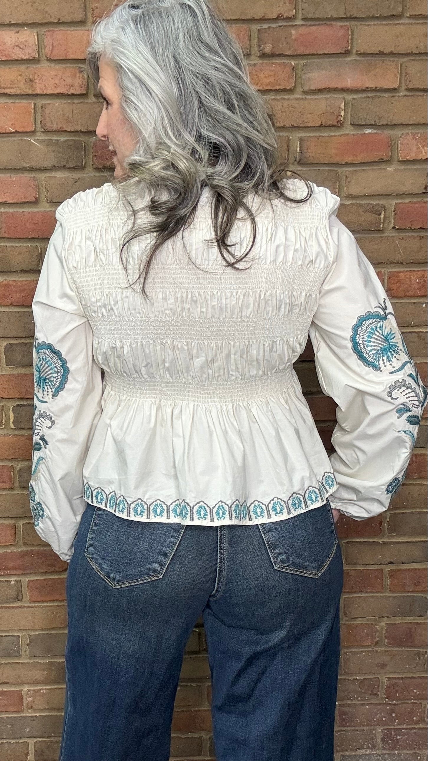 Woman wearing the Embroideried Smocked Peasant Top and Judy Blue Palazzo jeans against a brick wall.
