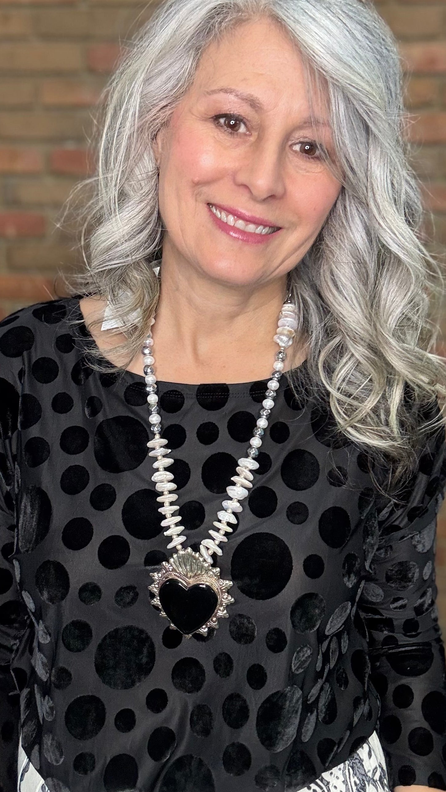 Woman wearing Black Velvet Burnout Top, Floral Print Wide Leg Pant against a brick wall. 