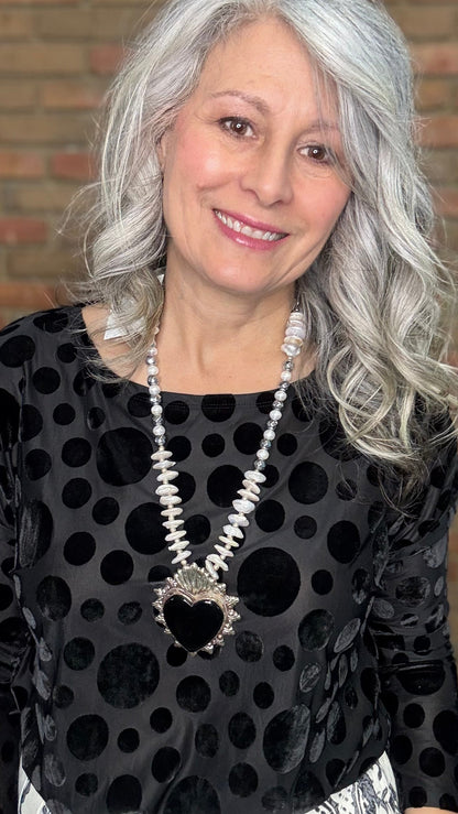 Woman wearing Black Velvet Burnout Top, Floral Print Wide Leg Pant against a brick wall. 