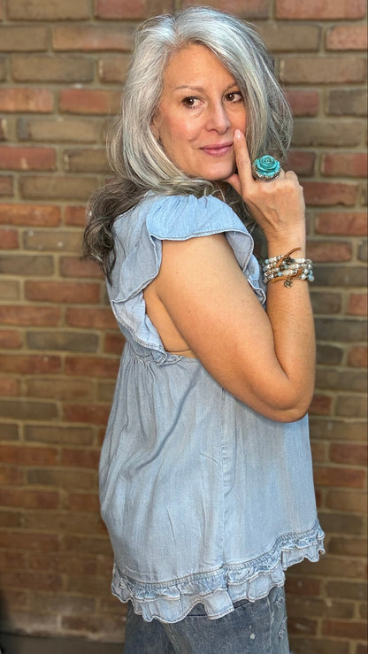 Woman with gray hair wearing a light blue dress against a brick wall.