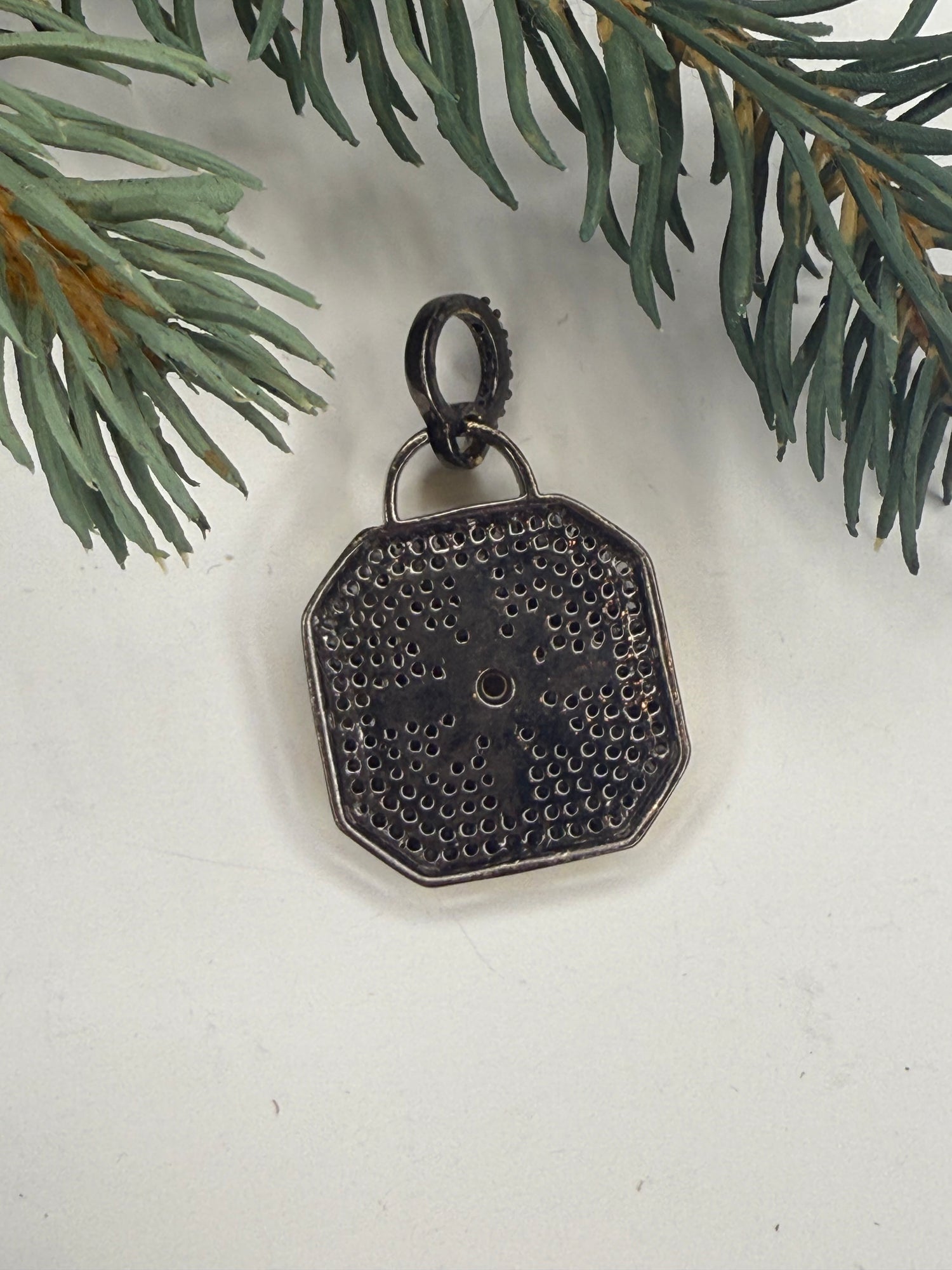 Back of Lock shaped pendant on a white surface with greenery