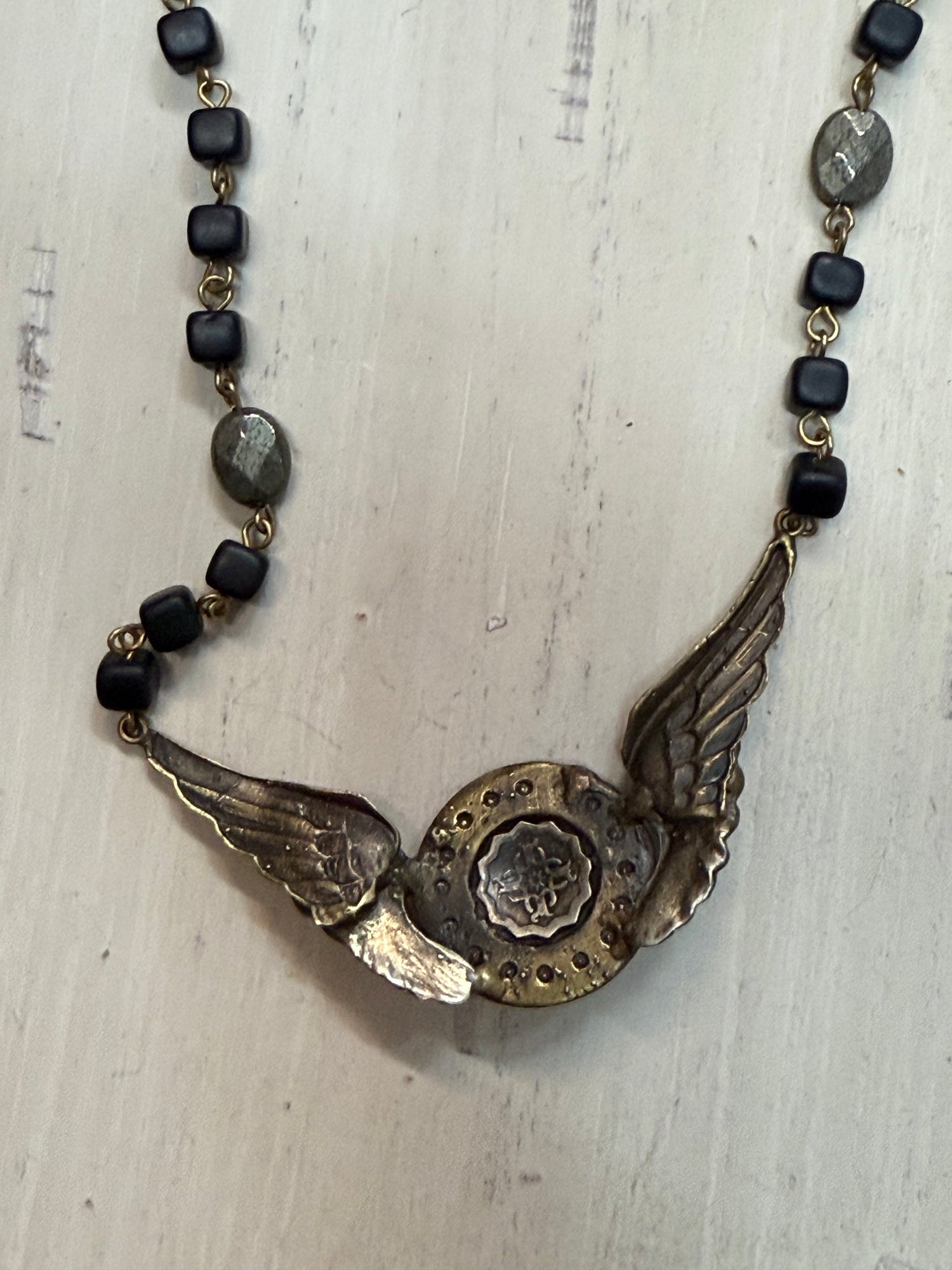 Back of Necklace with winged pendant and black beads on a textured surface
