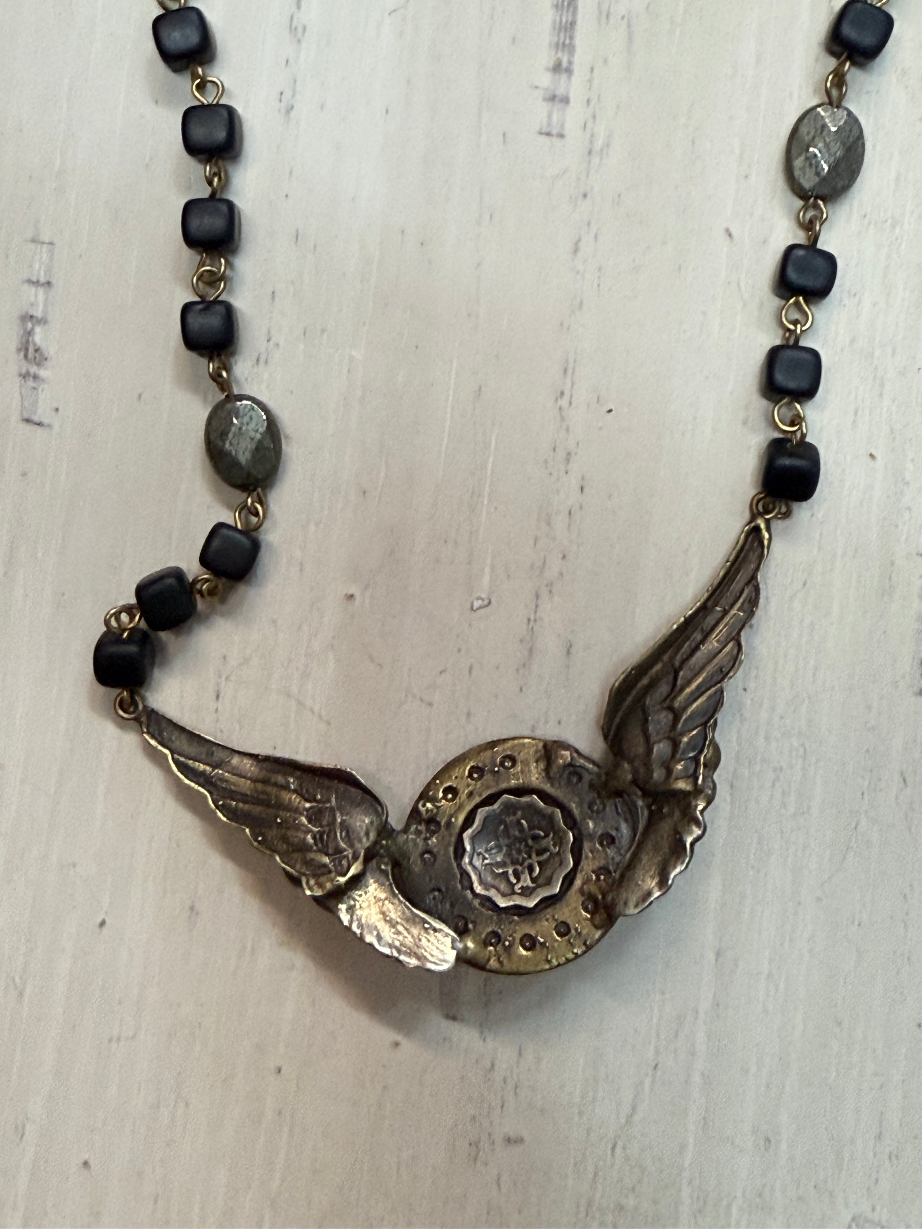Back of Necklace with winged pendant and black beads on a textured surface