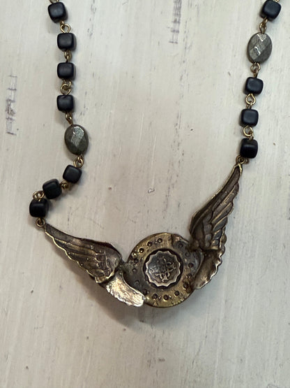 Back of Necklace with winged pendant and black beads on a textured surface