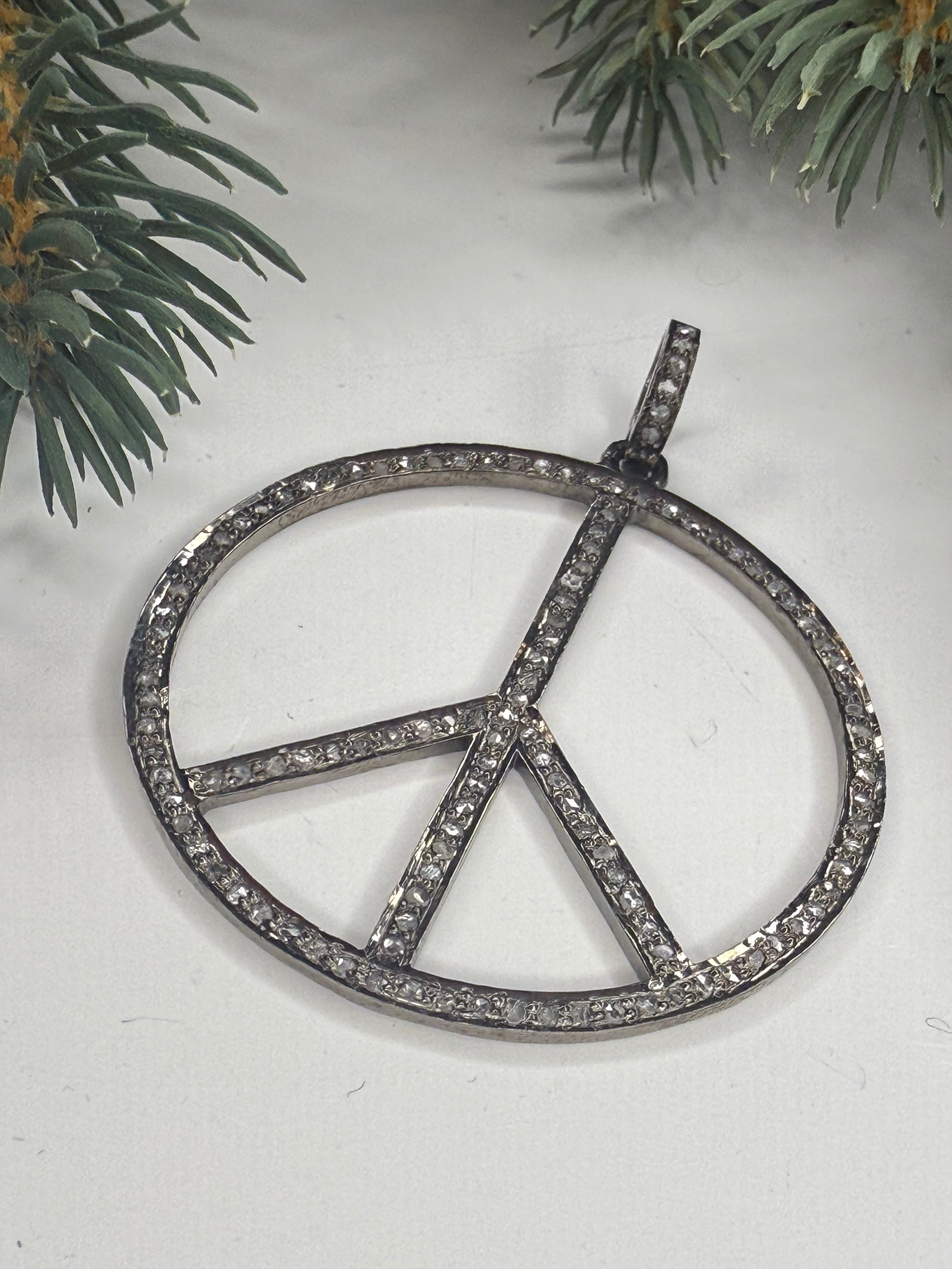 Peace sign pendant with pave diamonds on a white background with greenery