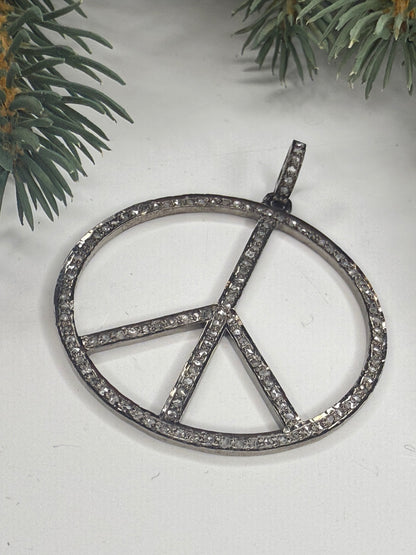 Peace sign pendant with pave diamonds on a white background with greenery