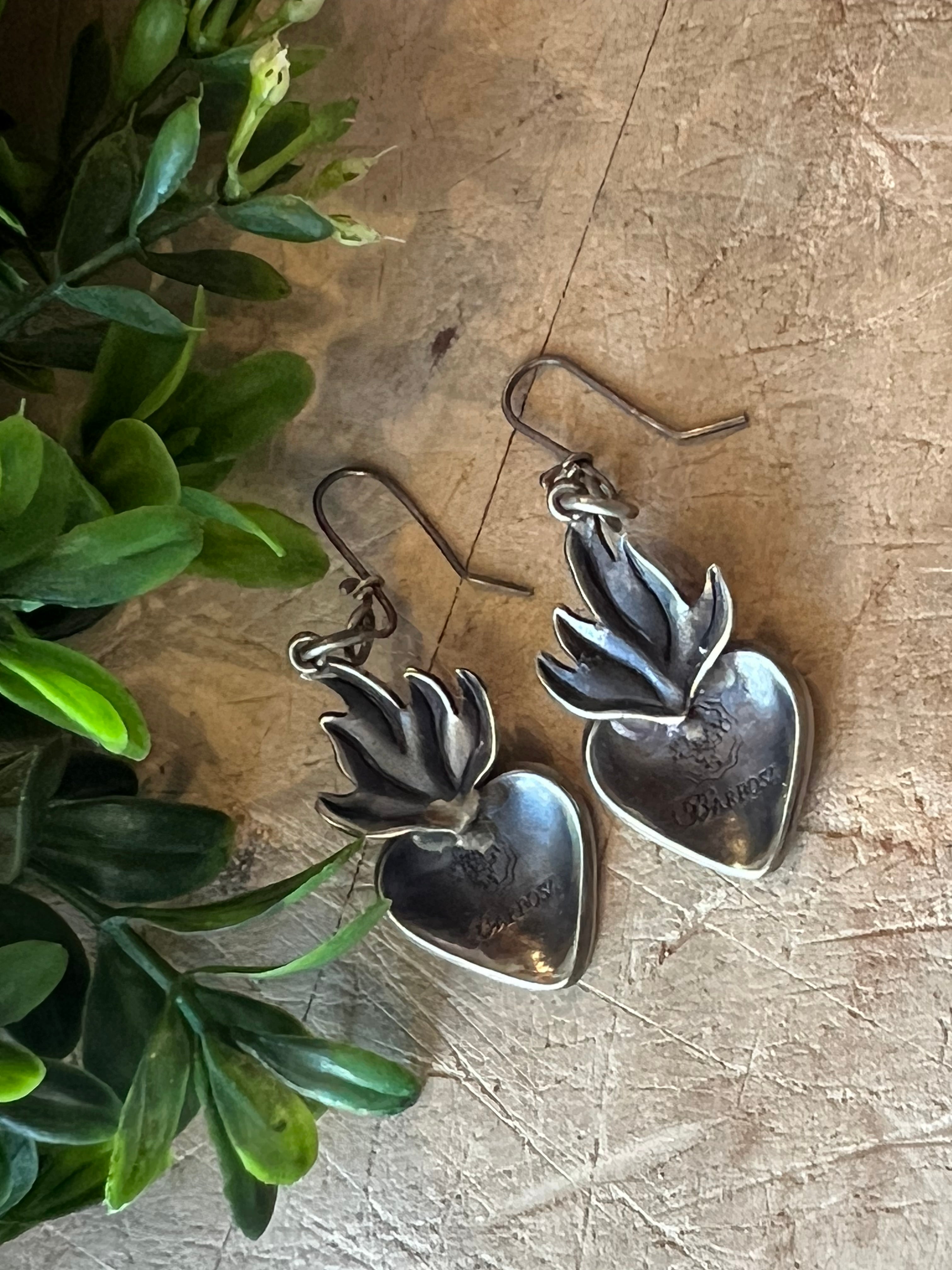 Small Flame Heart Earrings on a textured surface with greenery in the background