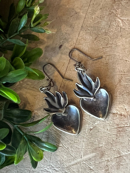 Small Flame Heart Earrings on a textured surface with greenery in the background
