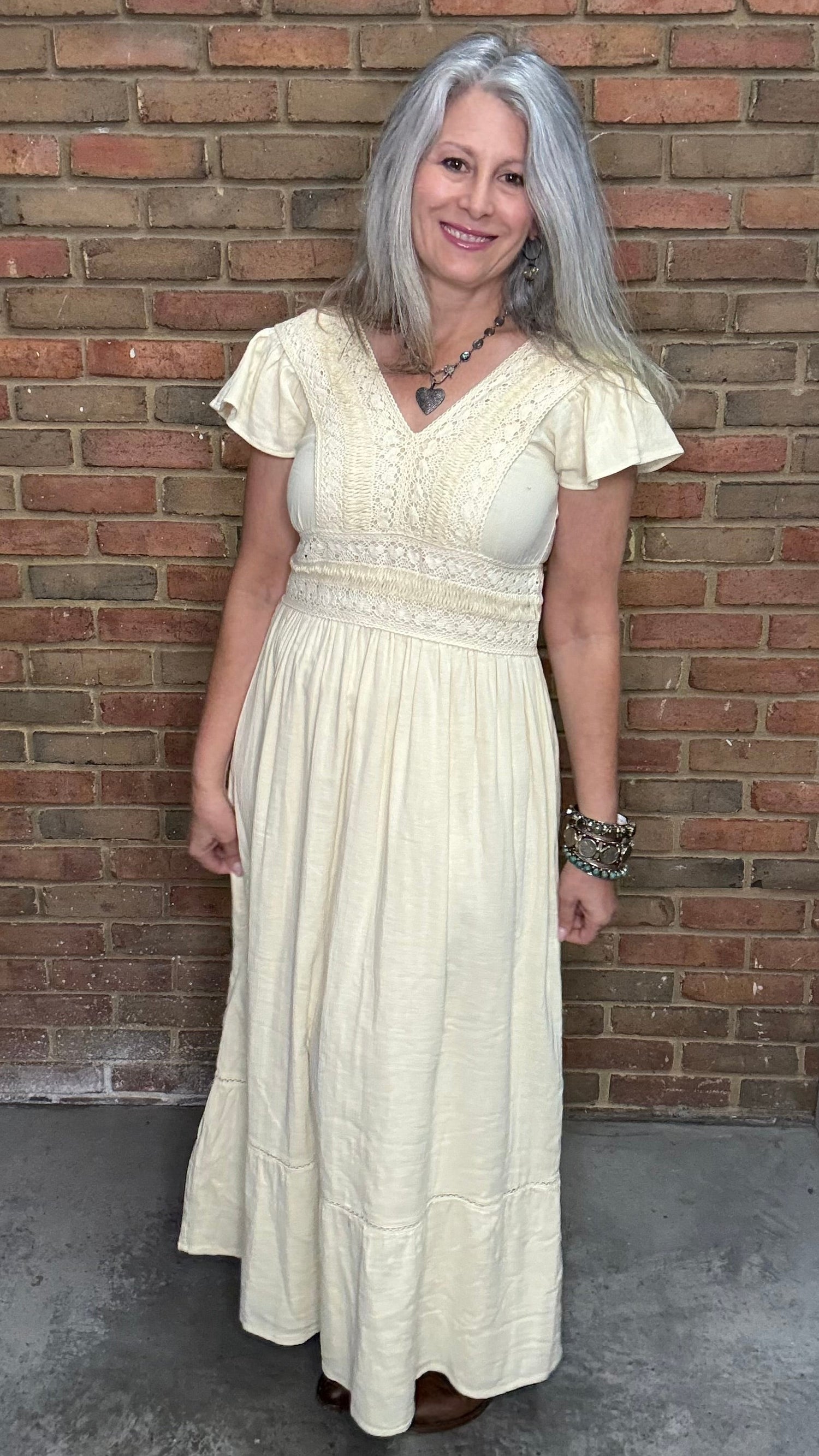 Woman in the Vina Cotton Lace Dress in Ivory standing against a brick wall