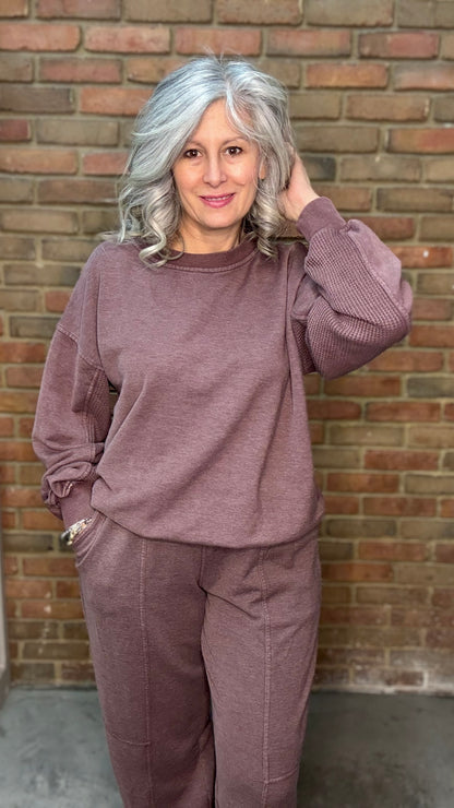 Woman in a mauve outfit standing against a brick wall