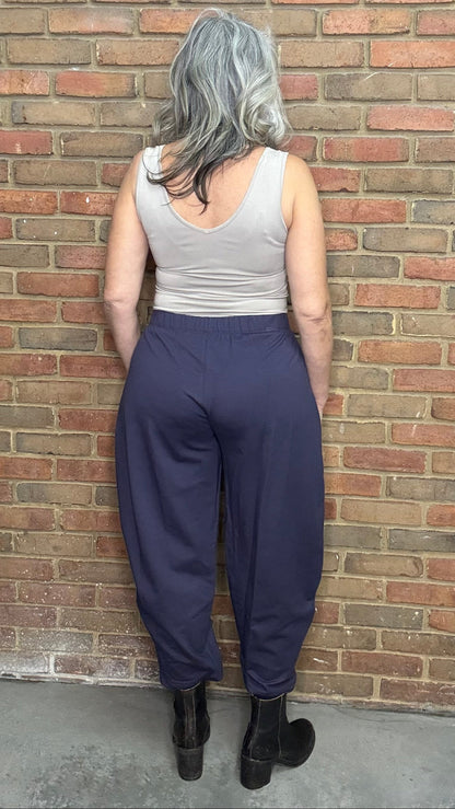 Woman standing against a brick wall wearing a tank top and the Mady Pant in plum.