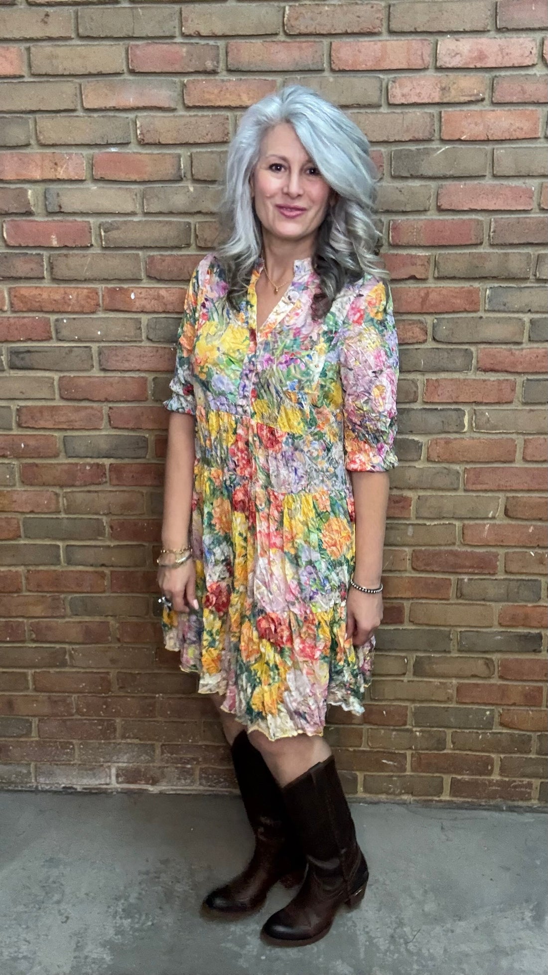 Woman in Garden Floral Print Tiered Dress and brown boots standing against a brick wall.
