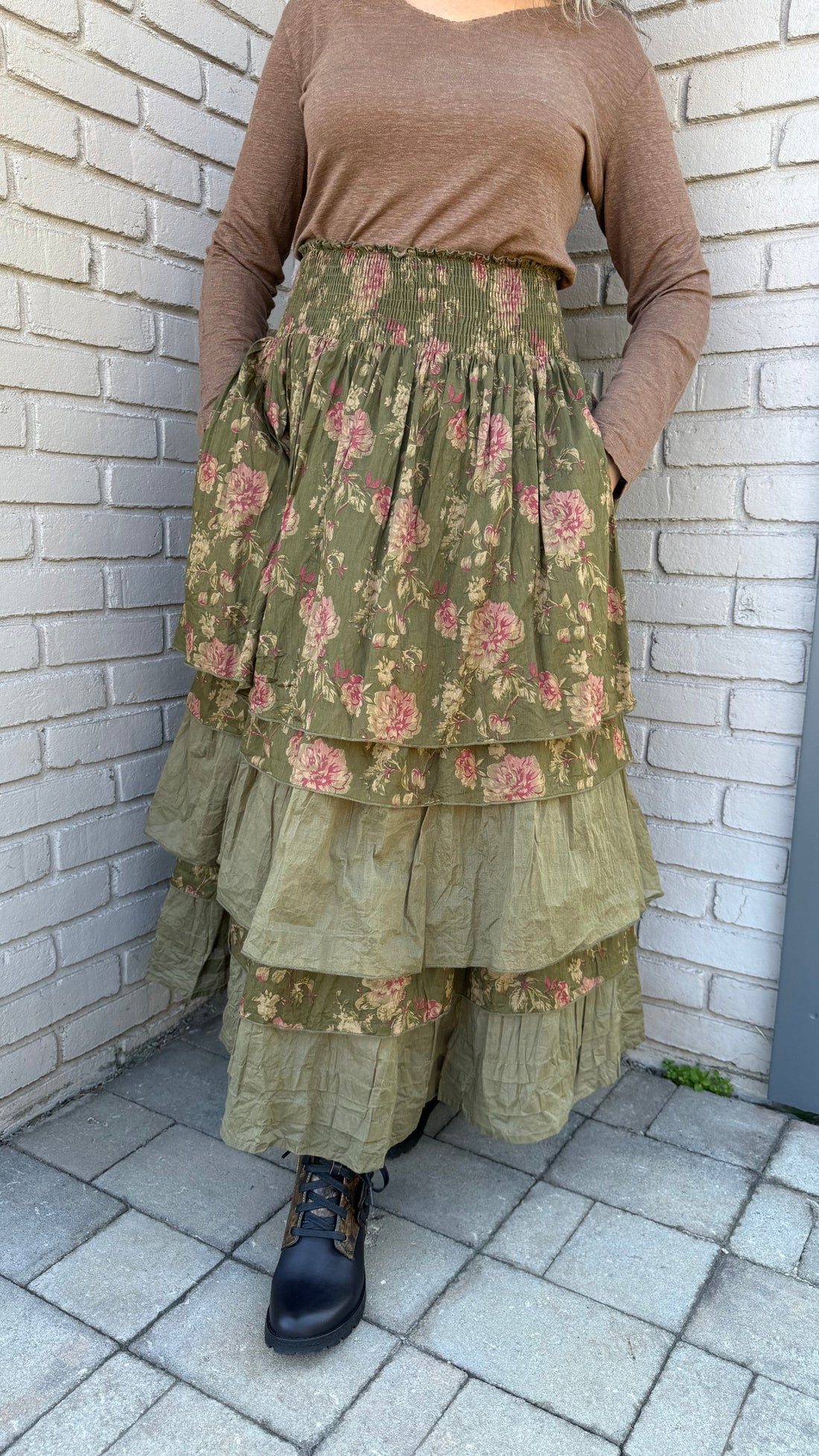 Person holding a green floral dress on a tiled pavement.