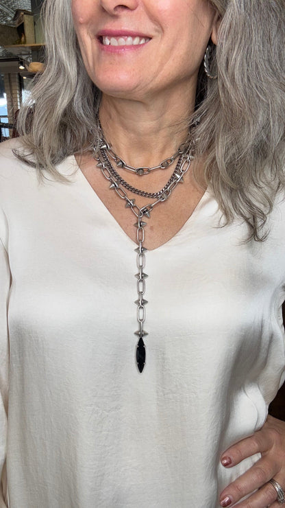 Person wearing a white top and silver necklace with a black pendant.