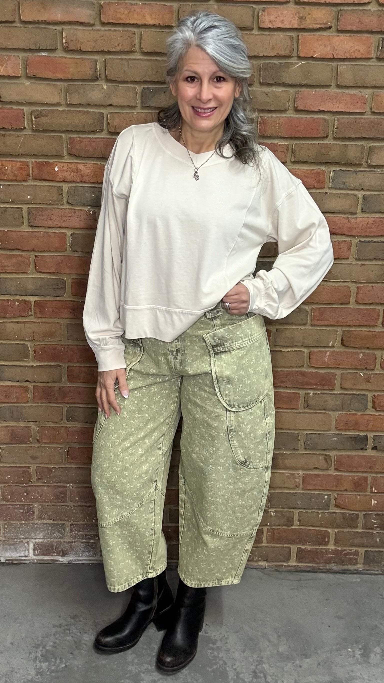 Woman standing against a brick wall wearing the Taupe Long Sleeve Top and Floral Printed Barrel Pants.
