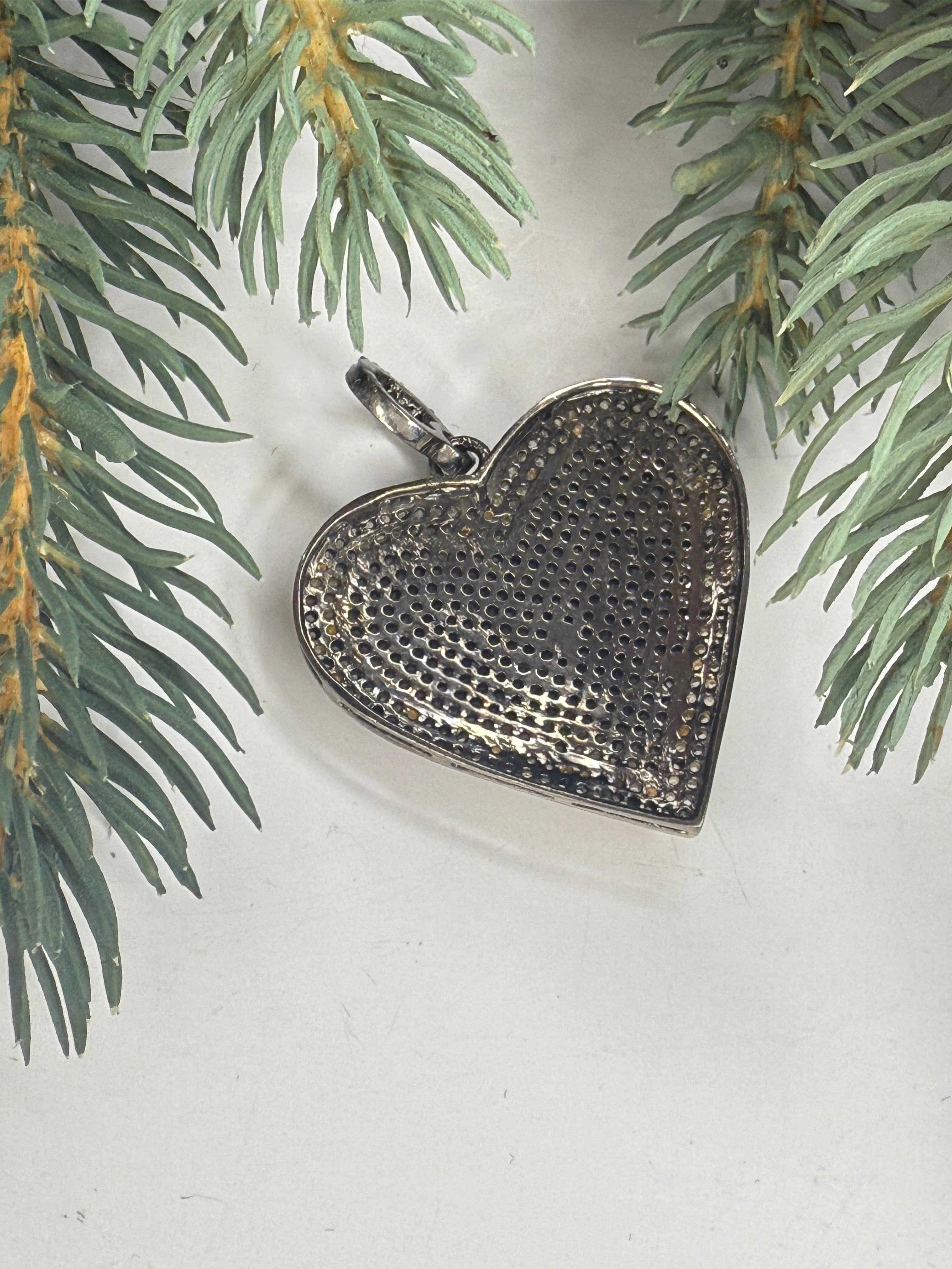 Back of Heart-shaped silver pendant on a light background with greenery