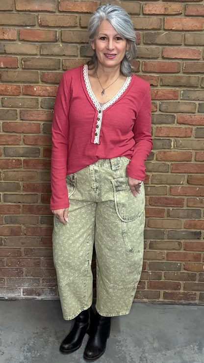 Person wearing the Raspberry Rose Ribbed Henley long-sleeve Top with the Floral Printed Barrel Pants against a brick wall.