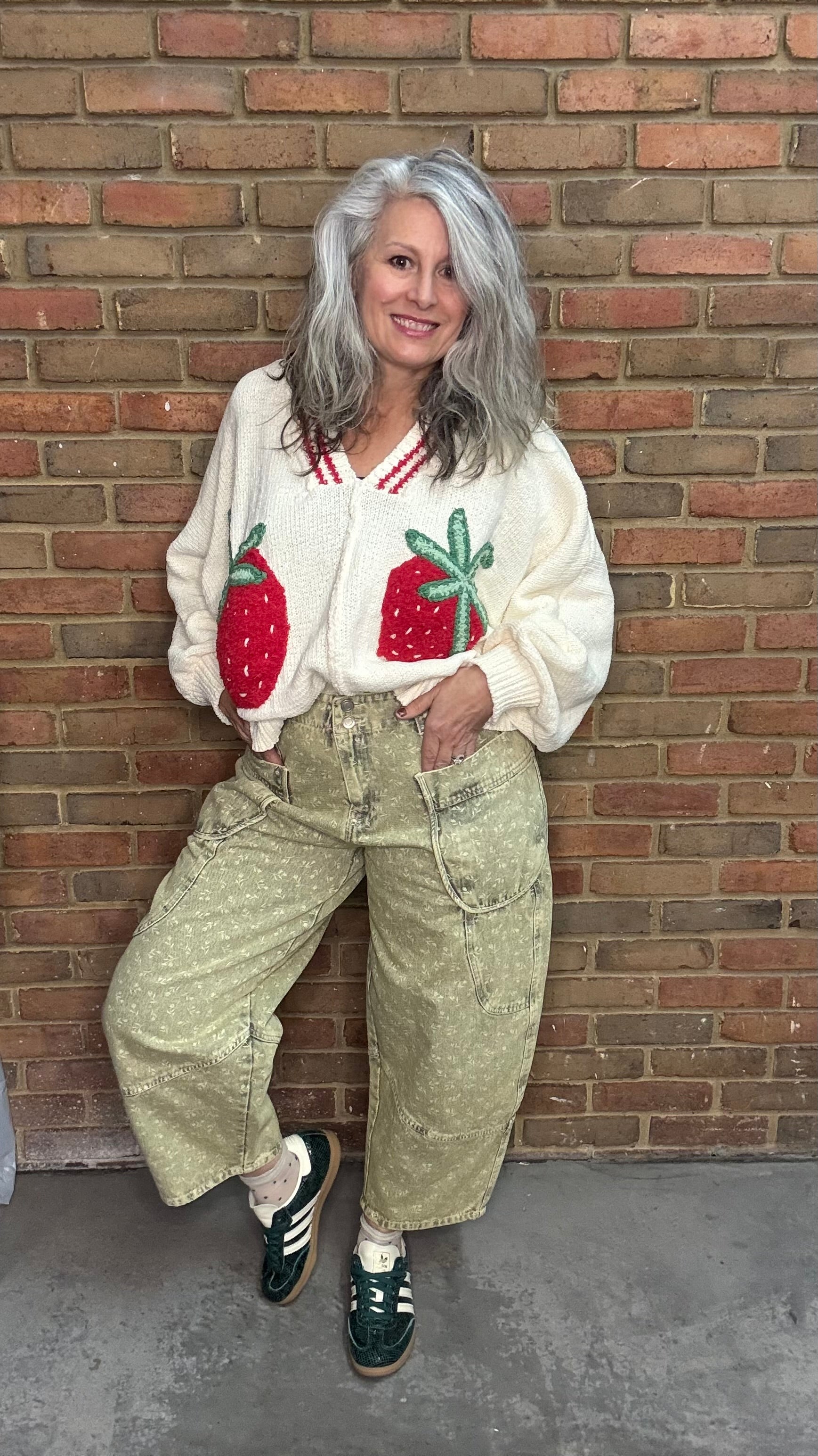 Person wearing a white sweater with strawberry designs against a brick wall.