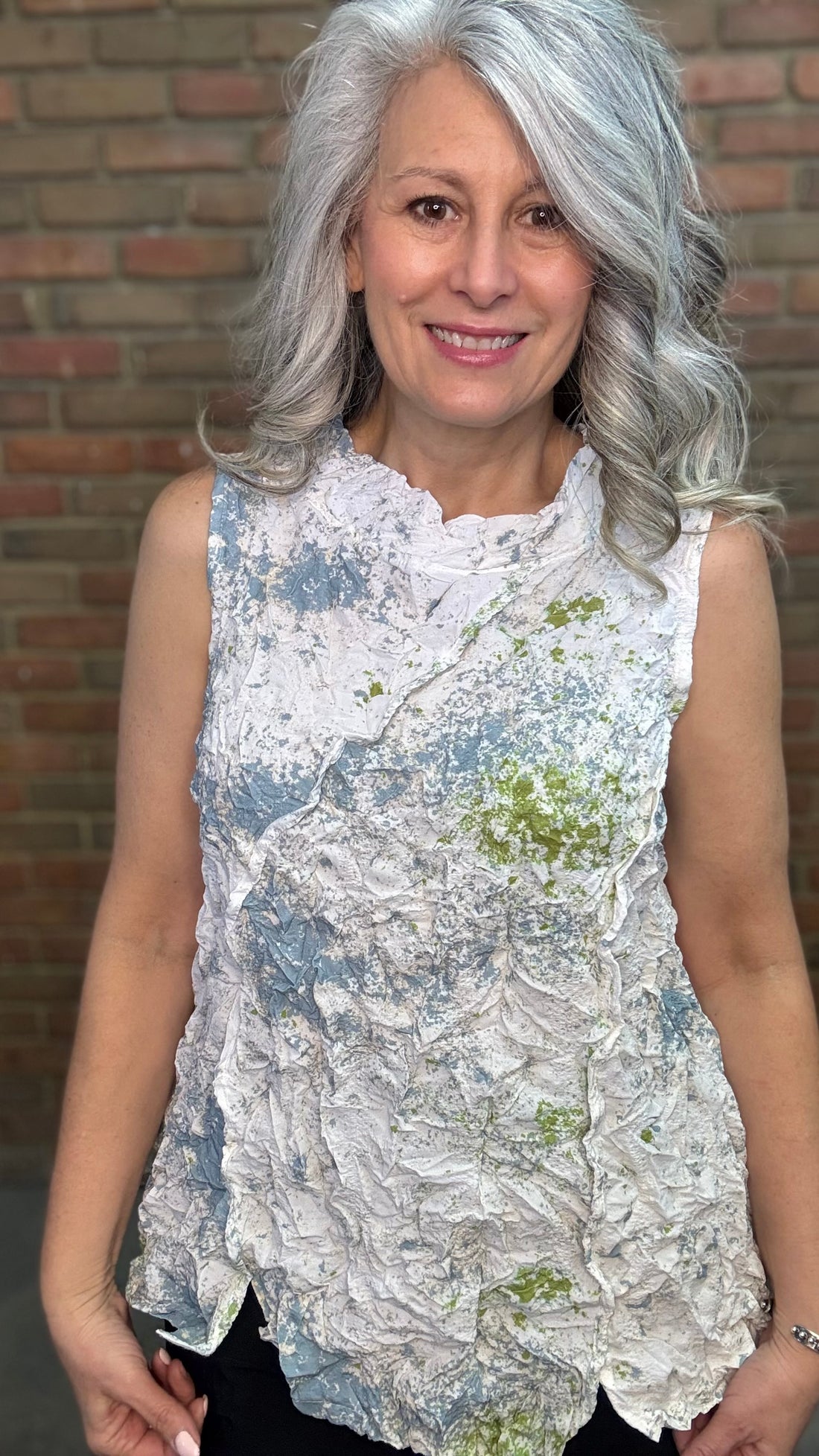Woman standing against a brick wall wearing Levana Tank - Fiji and black pants.
