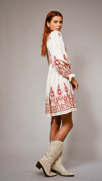 Woman wearing a white dress with red embroidery and white boots on a gray background