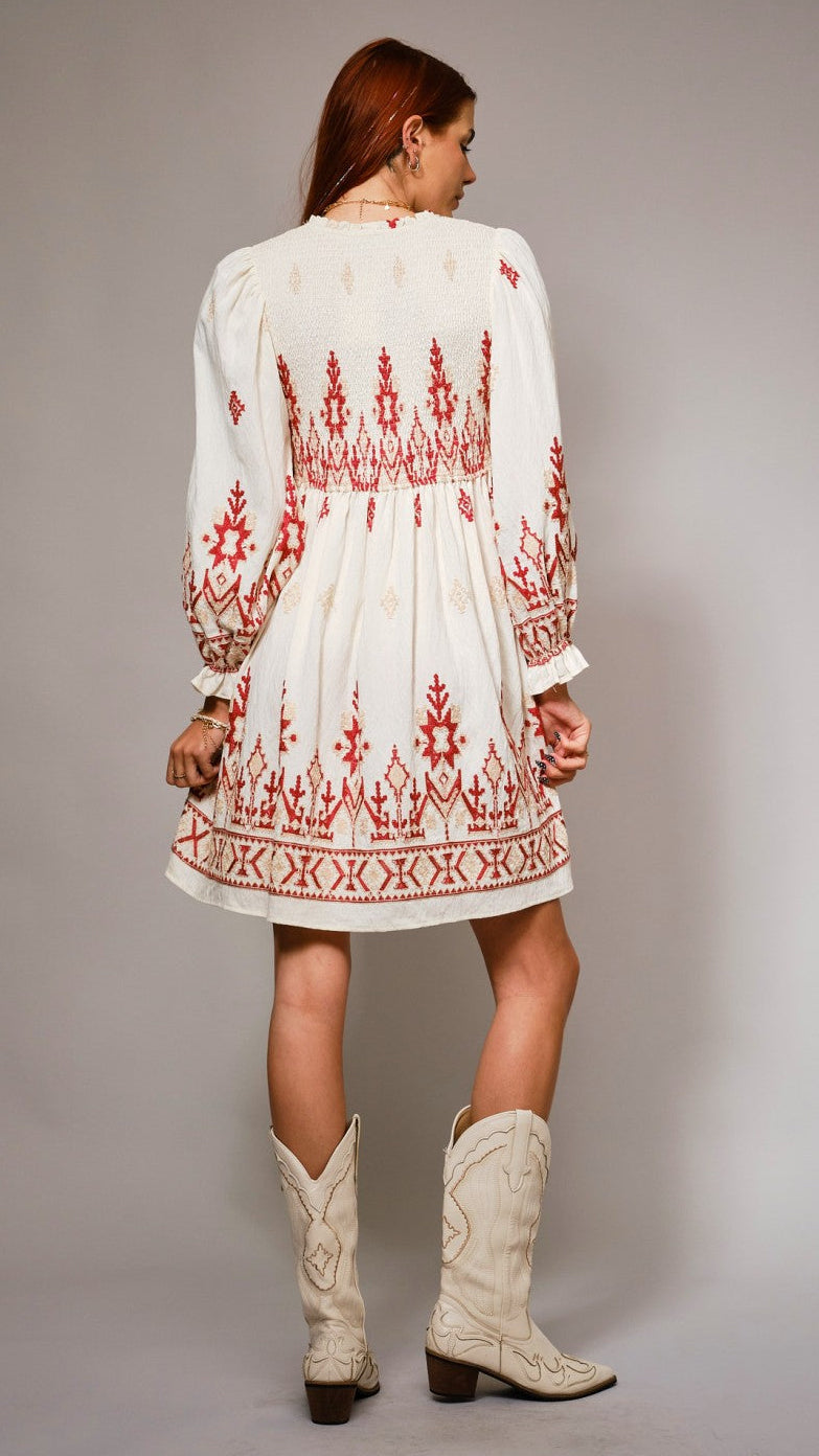 Woman wearing a white dress with red embroidery and white cowboy boots on a gray background