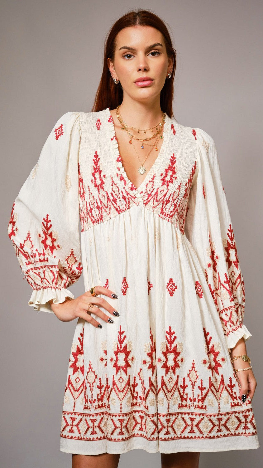 Woman wearing a white dress with red embroidery against a gray background