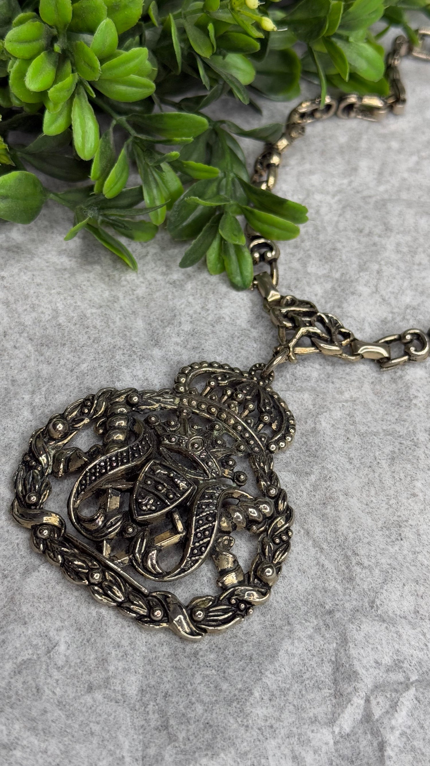 Decorative heart-shaped necklace on a textured surface with greenery