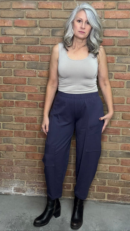 Woman standing against a brick wall wearing a tank top and the Mady Pant in plum.