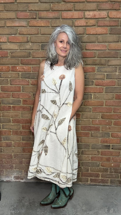 Woman in a white dress with floral patterns leaning against a brick wall.