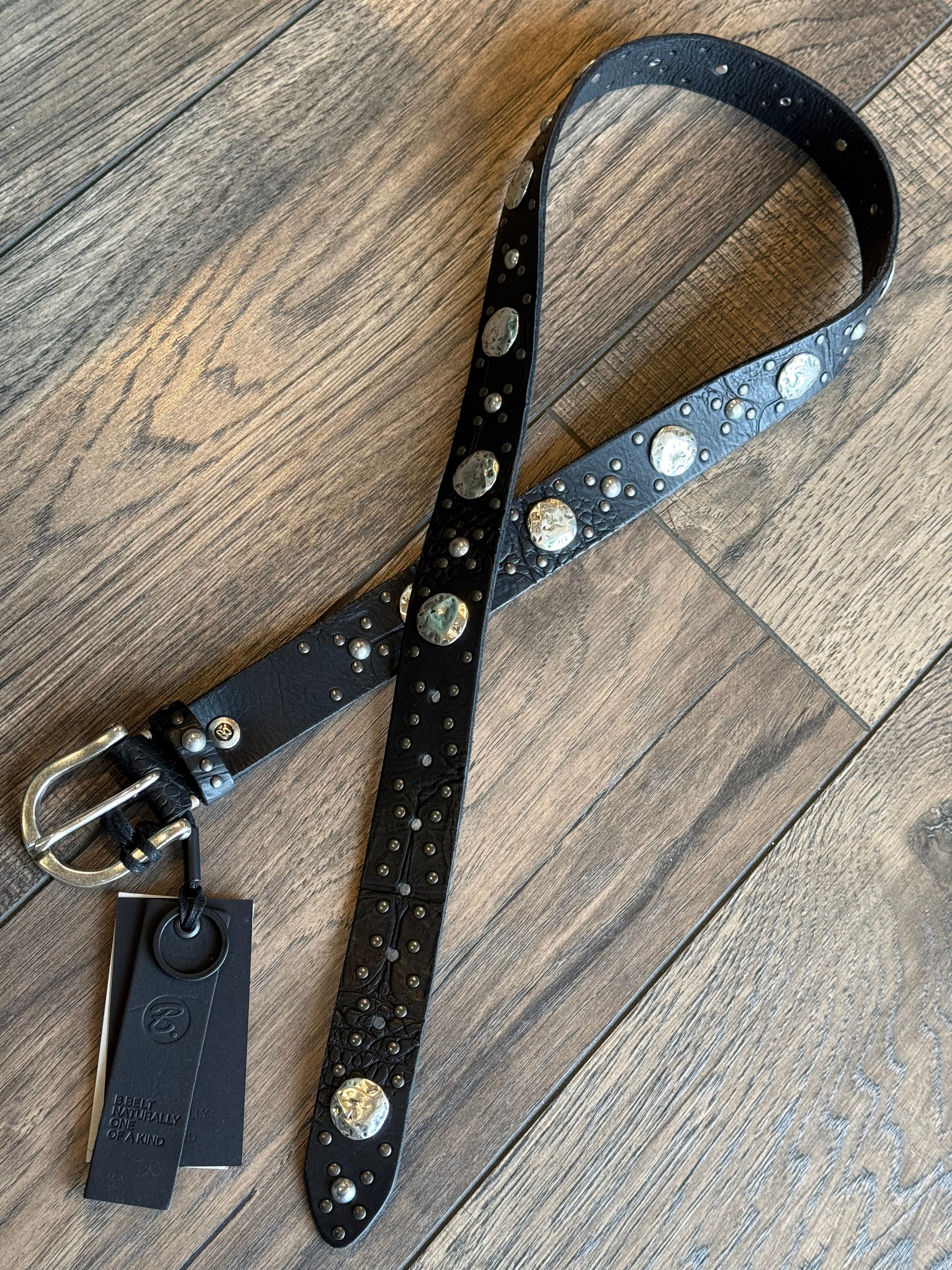 Black leather belt with silver studs and a metal buckle on a wooden surface