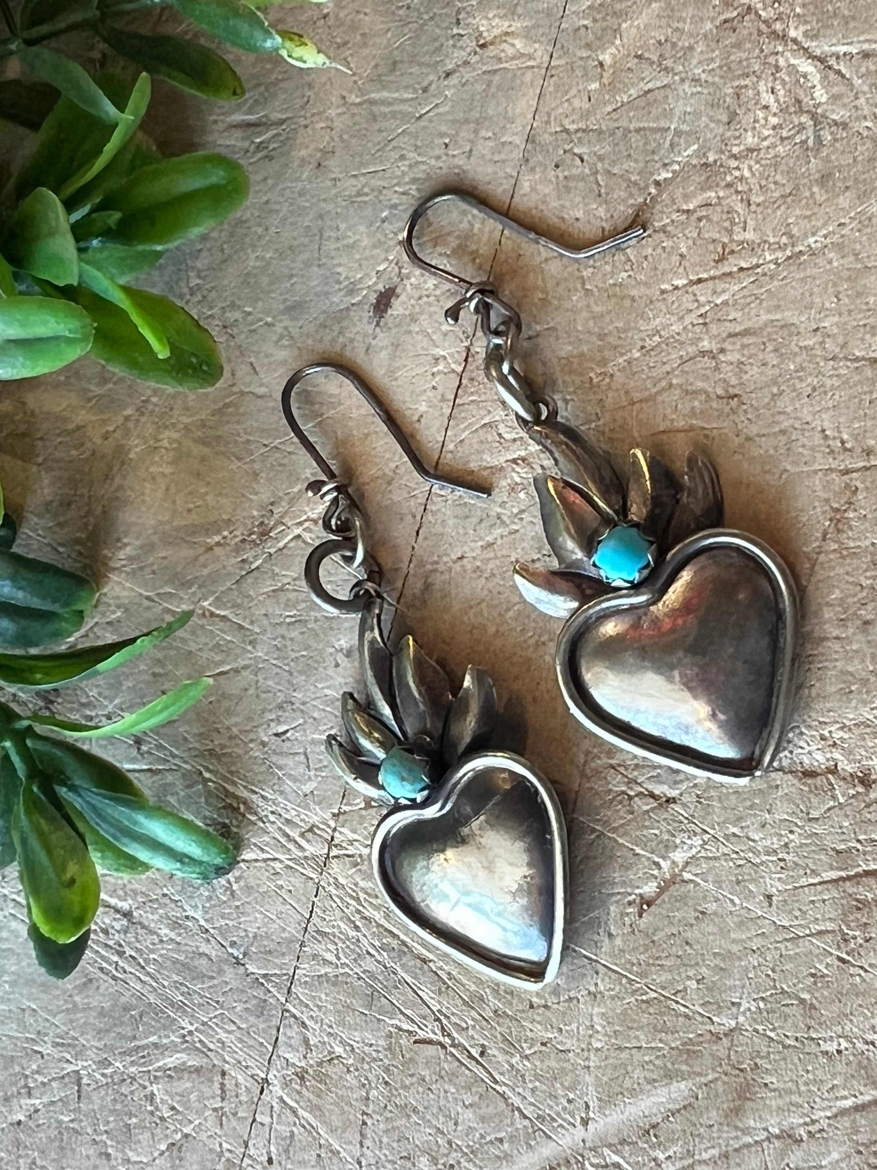 Small Flame Heart Earrings on a textured surface with greenery in the background
