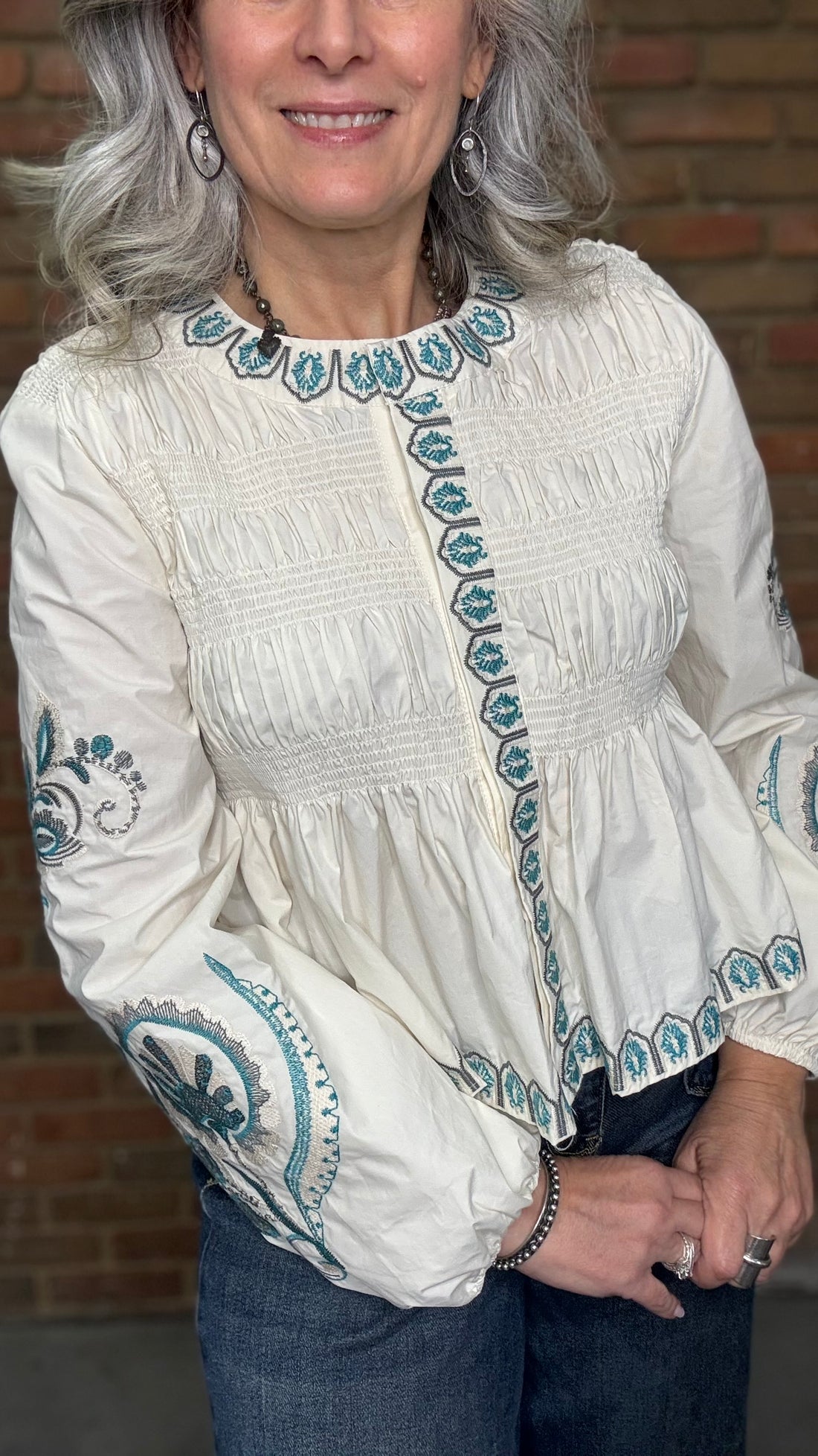 Woman wearing the Embroideried Smocked Peasant Top and Judy Blue Palazzo jeans against a brick wall.