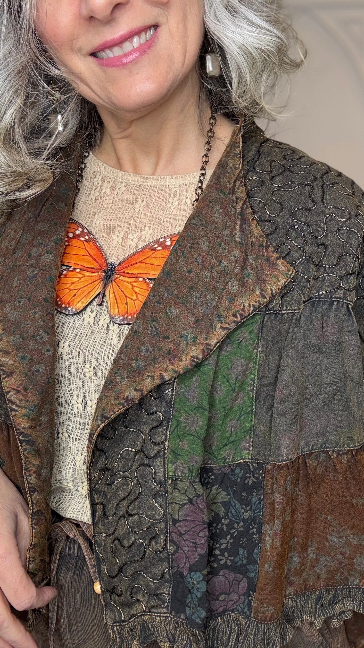 Woman wearing Boho Embroidered Lapel Crop Jacket, beige lace top with Monarch Butterfly Necklace and Amber Boho Chic pants against a white paneled wall.