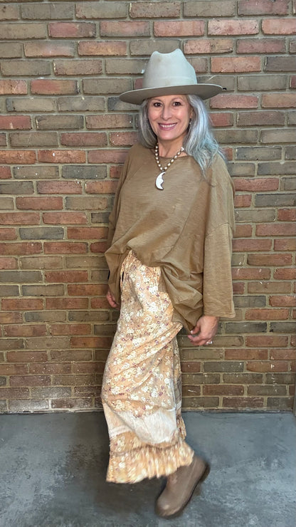 Woman wearing Be Free Top - Vintage Latte and patterned pants against a brick wall.